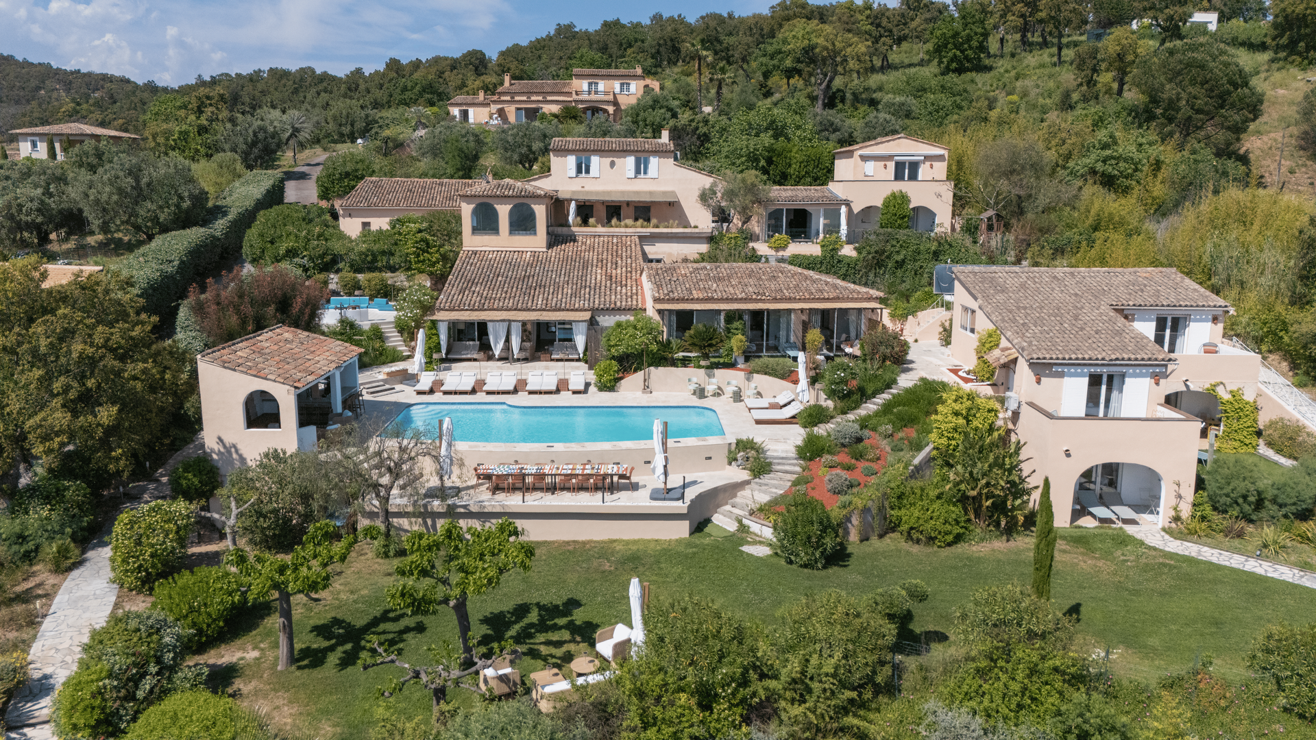 Luxury villas with pool on a hillside under a blue sky, lush greenery.