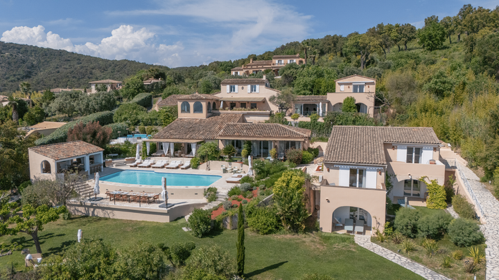 Luxury villas with pool on a hillside under a blue sky, lush greenery.