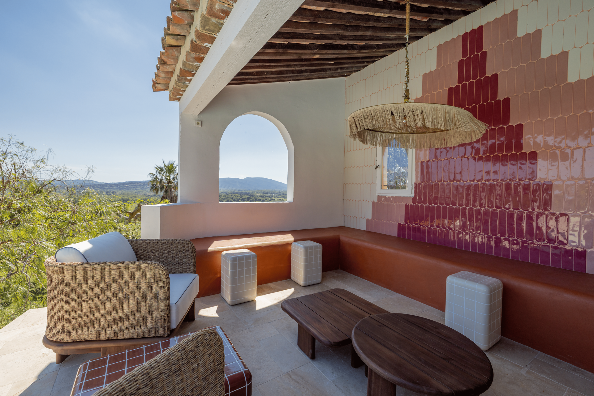 Outdoor bar with turquoise tile, pink wall, and woven light fixtures.