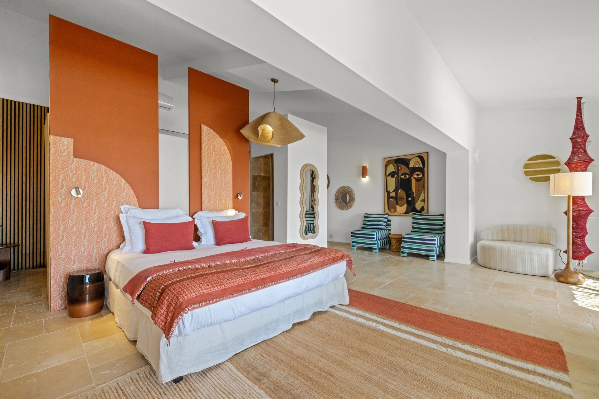 Bedroom with rust-colored accent wall, bed with white linens, and seating area with art and decorative objects.