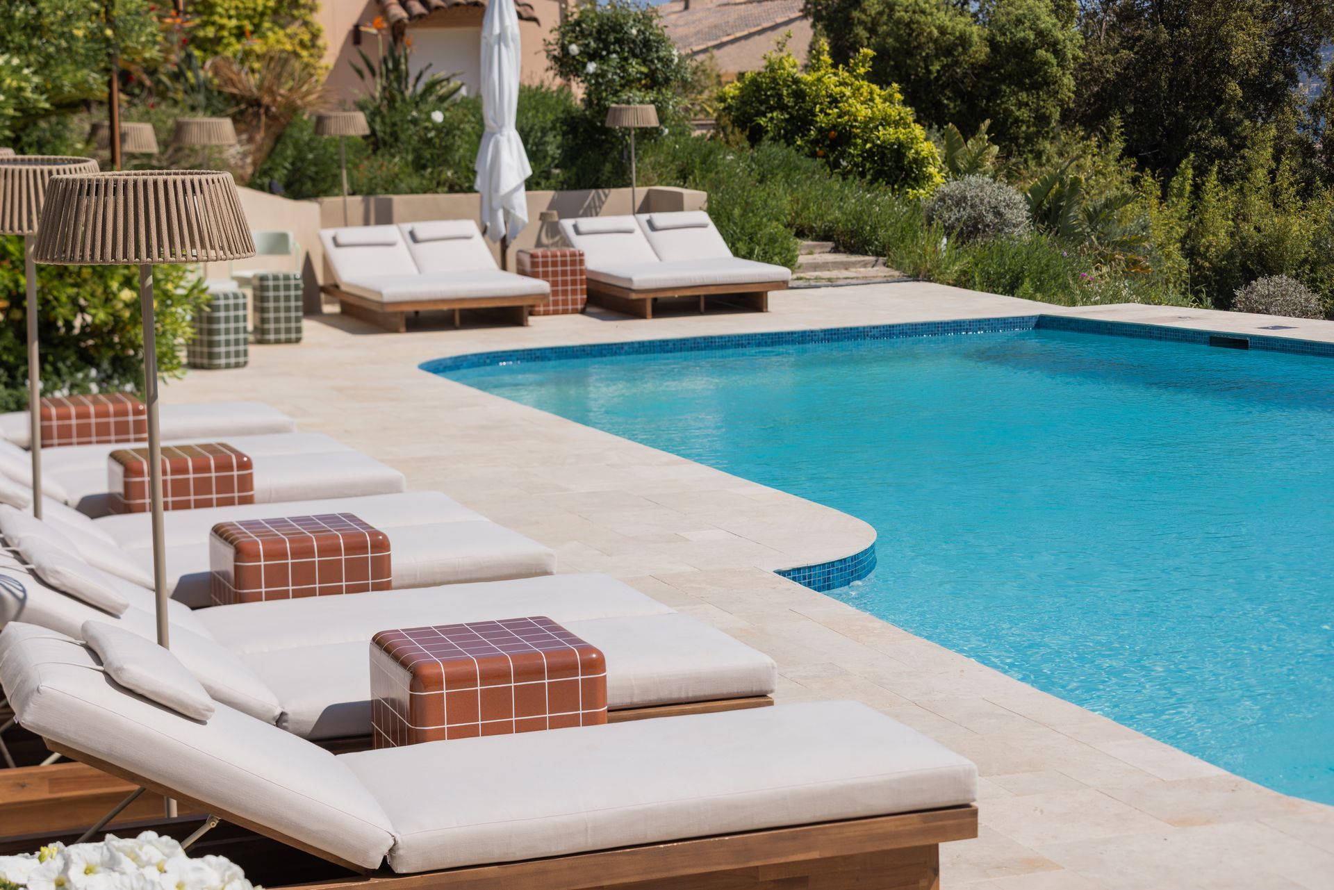 A swimming pool with lounge chairs and a yellow umbrella, overlooking a town on a sunny day.