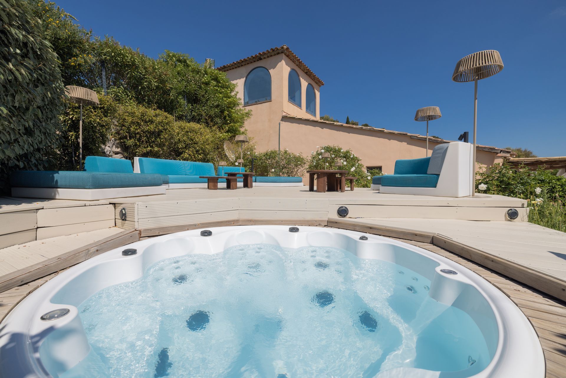 Hot tub with bubbling water on blue deck, overlooking a pool and ocean on a sunny day.