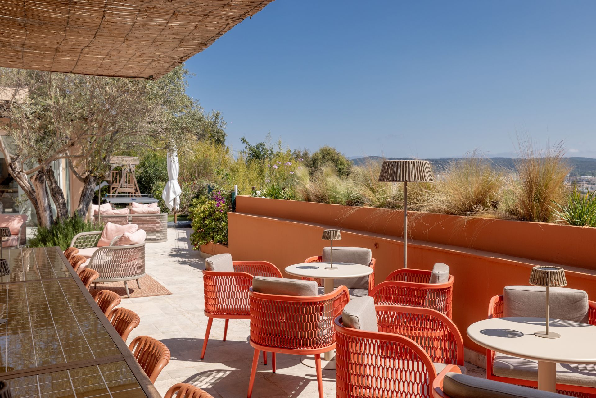 Outdoor patio with pink seating, table, and woven canopy, overlooking a scenic view.