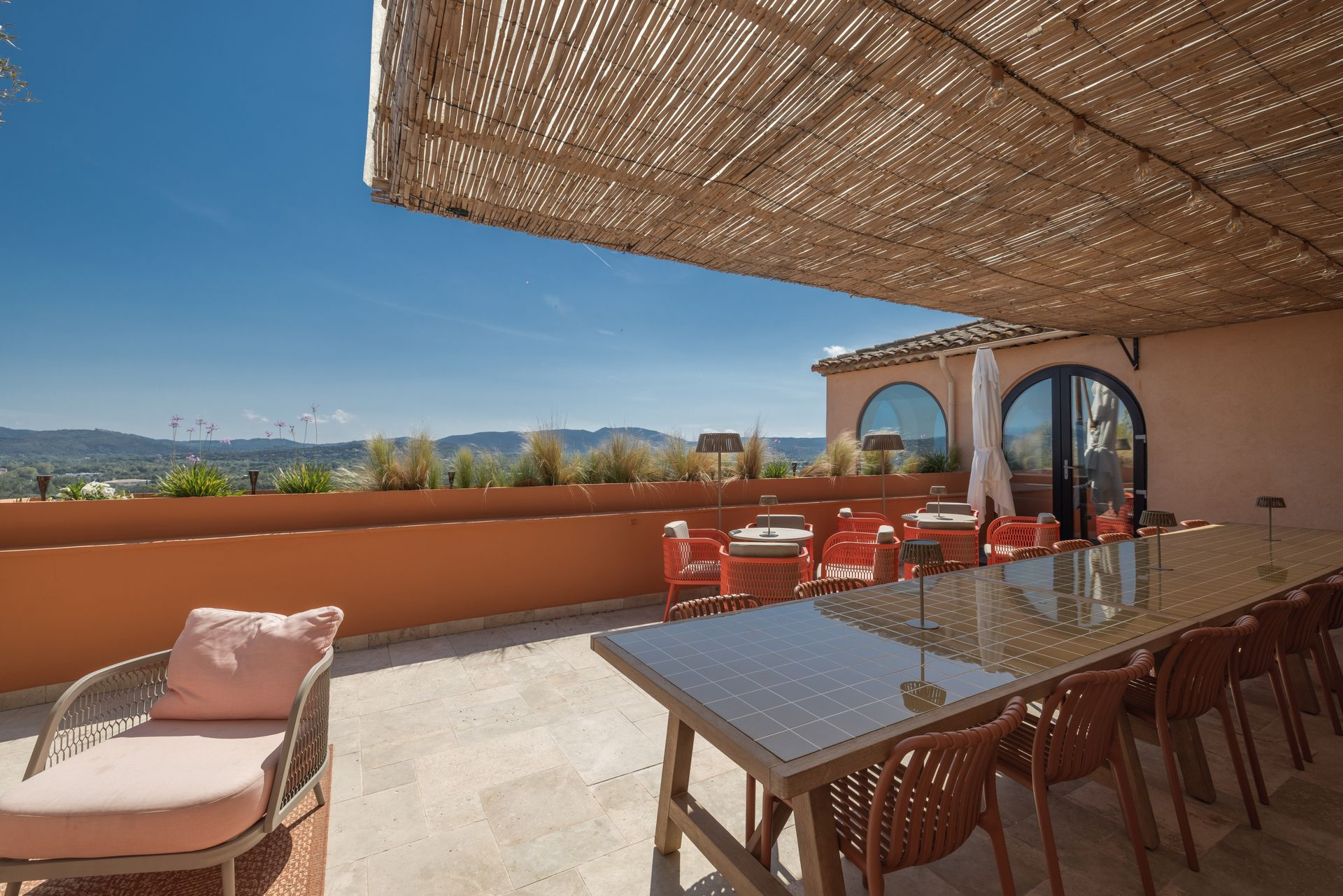 Outdoor patio with wicker furniture, pink cushions, and a woven canopy. Orange wall and tree branch.
