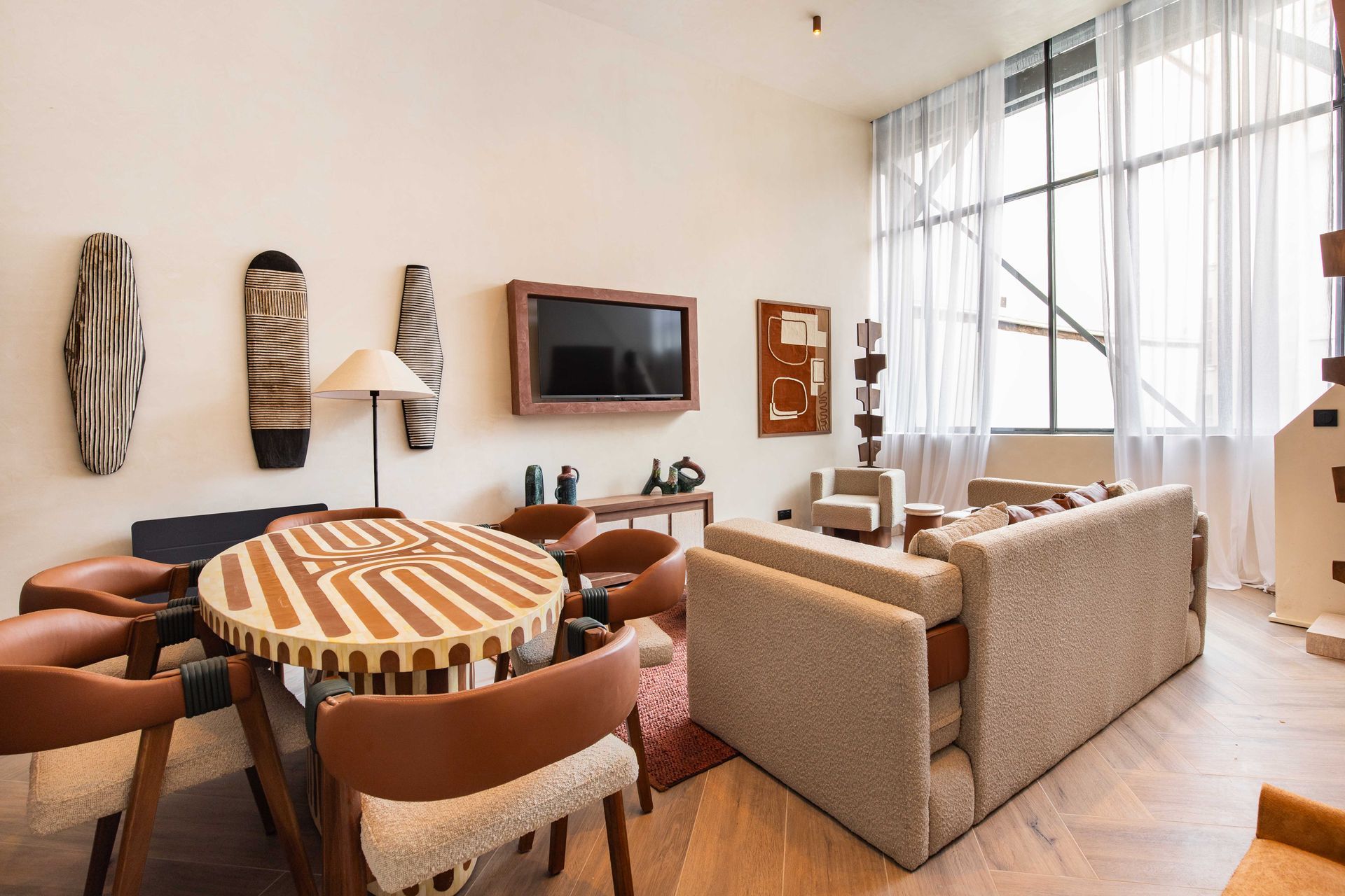 Living room with light beige sofa, round patterned table, and large window with white curtains.