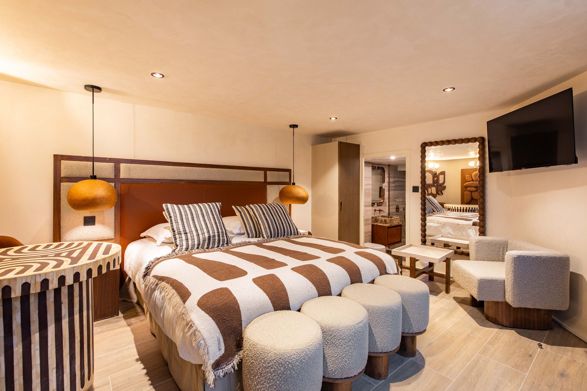 Cozy bedroom with a king bed, patterned blanket, seating area, and wall-mounted TV.