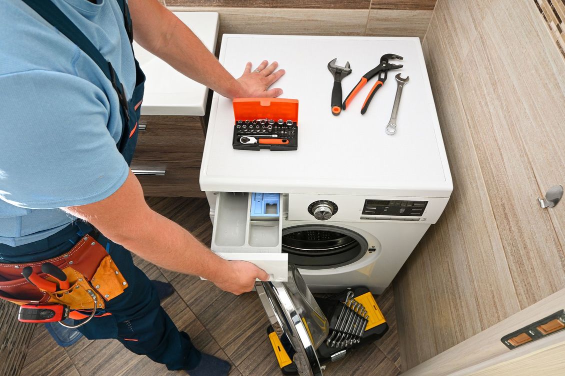 Un technicien répare une machine à laver, avec plusieurs outils posés sur le dessus de la machine.