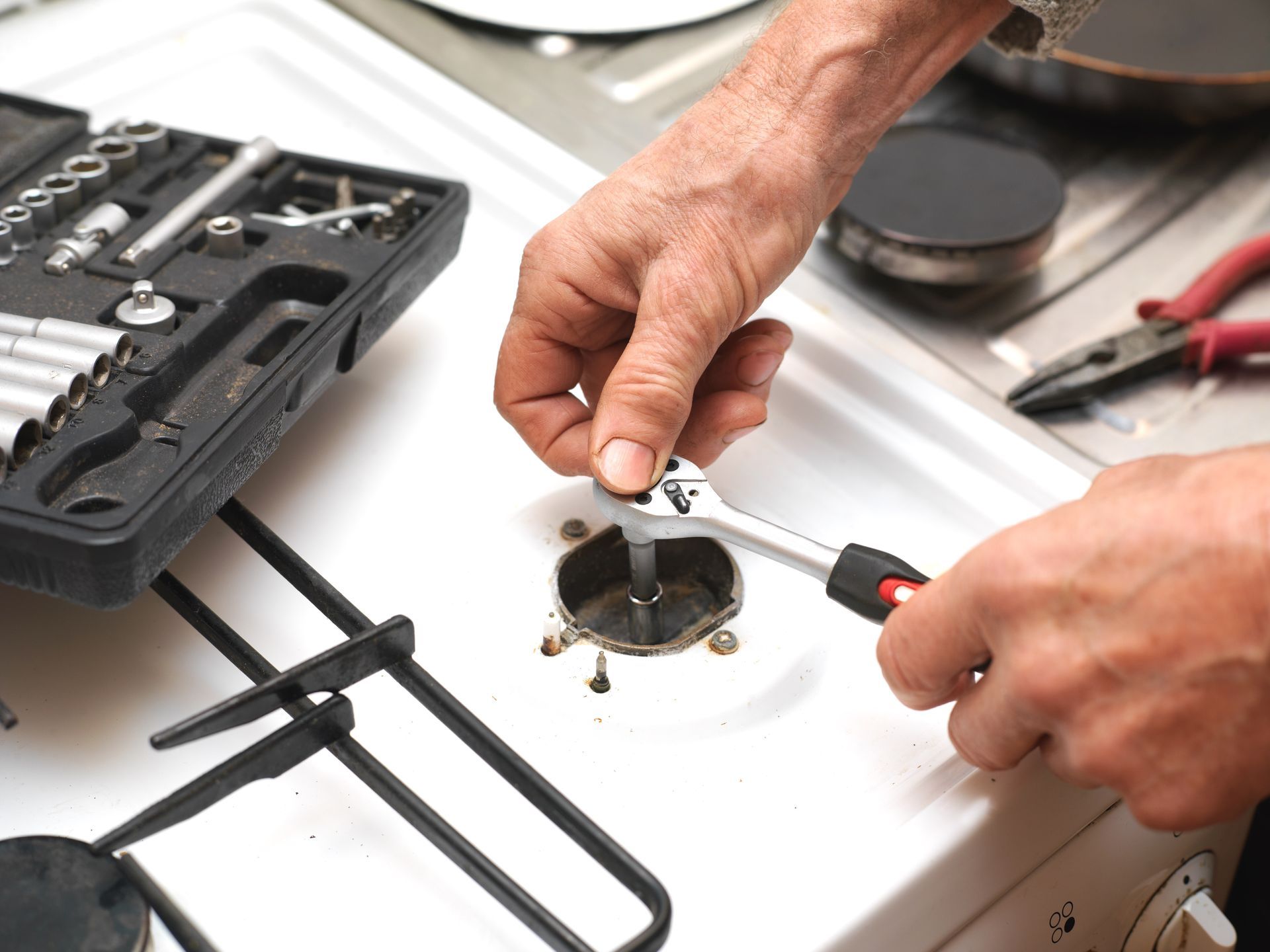 Des mains réparent une plaque de cuisson blanche avec des outils et un kit de réparation ouvert à côté.