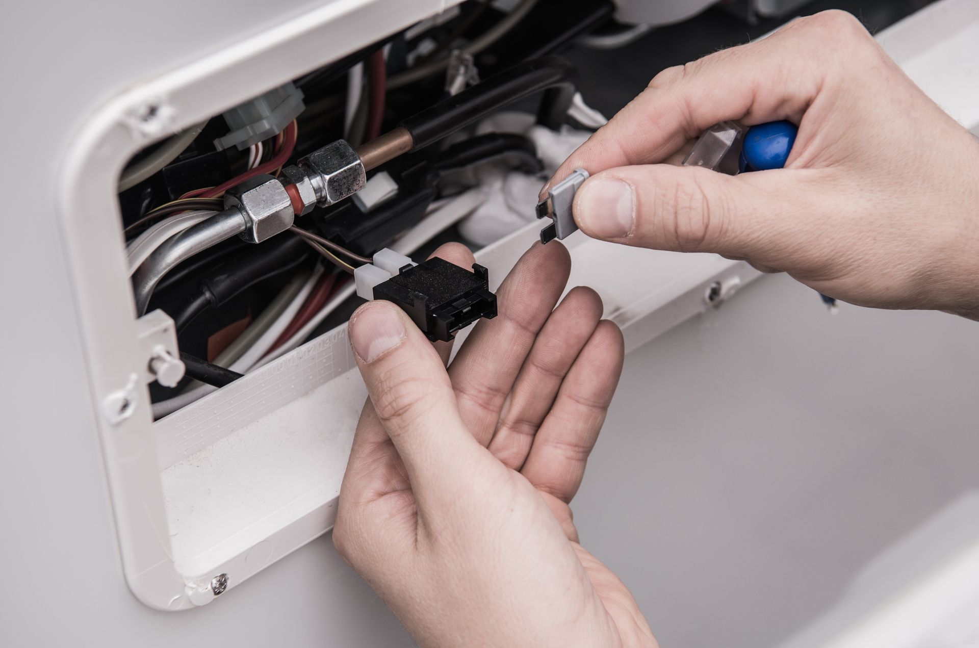 Des mains utilisent des pinces pour réparer des fils dénudés à l'intérieur d'un panneau électrique blanc.