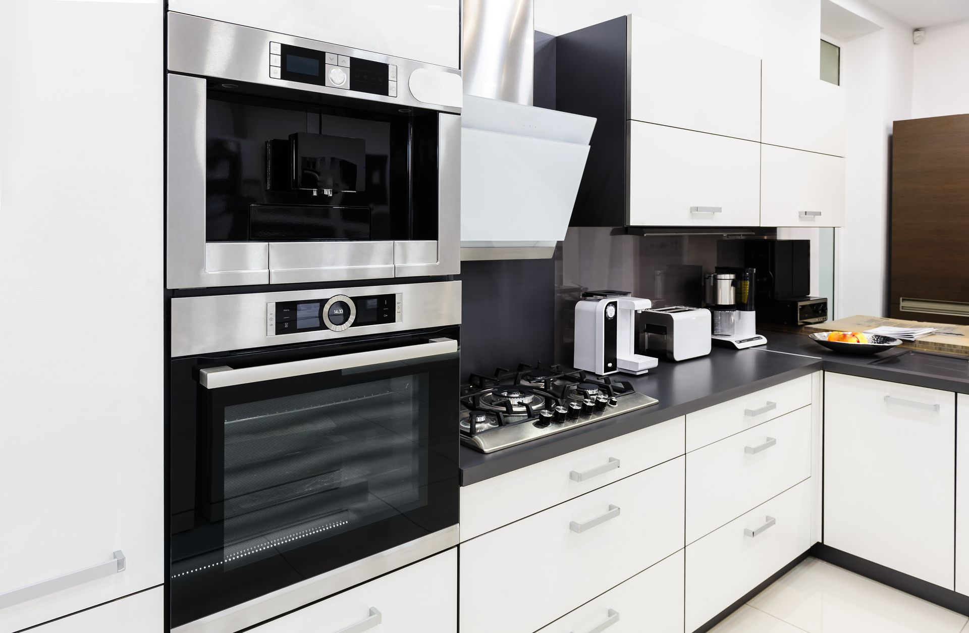 Cuisine blanche moderne avec four encastré, plaque de cuisson et appareils électroménagers sur le comptoir.