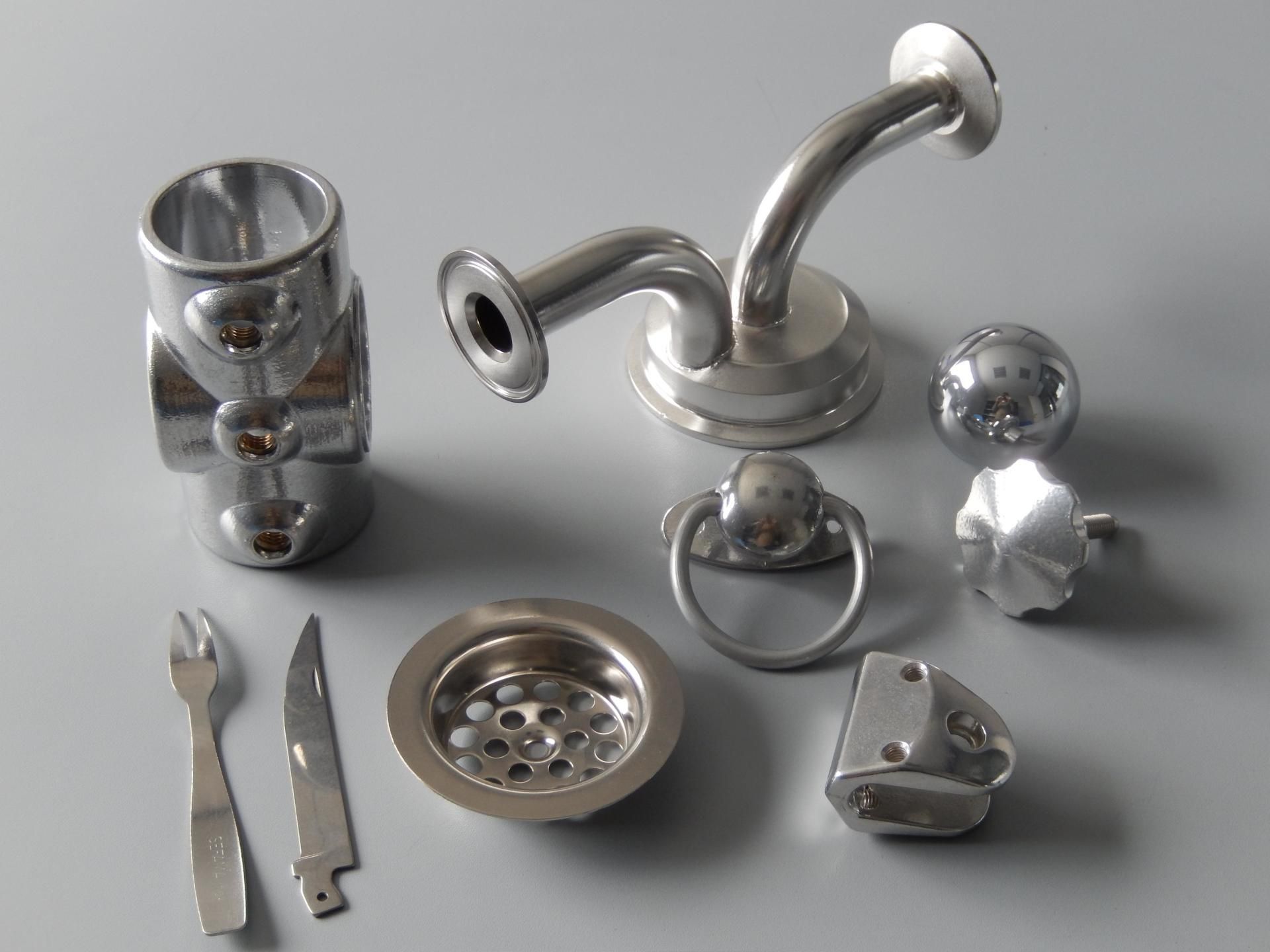 Collection de pièces et d'ustensiles de plomberie en métal brillant, disposés sur une surface grise.