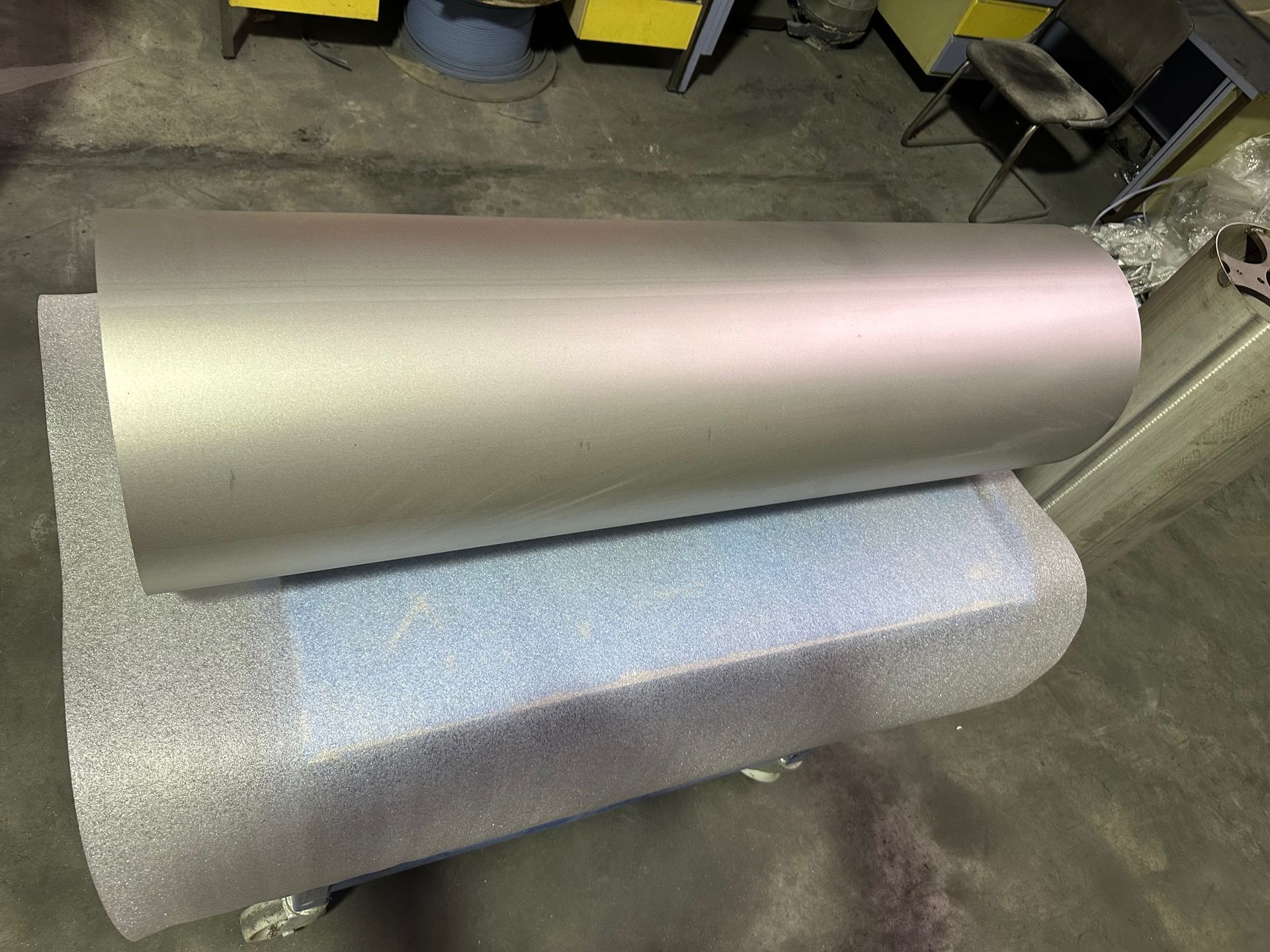 Tôle de métal argentée enroulée sur un support en mousse bleu clair dans un atelier.