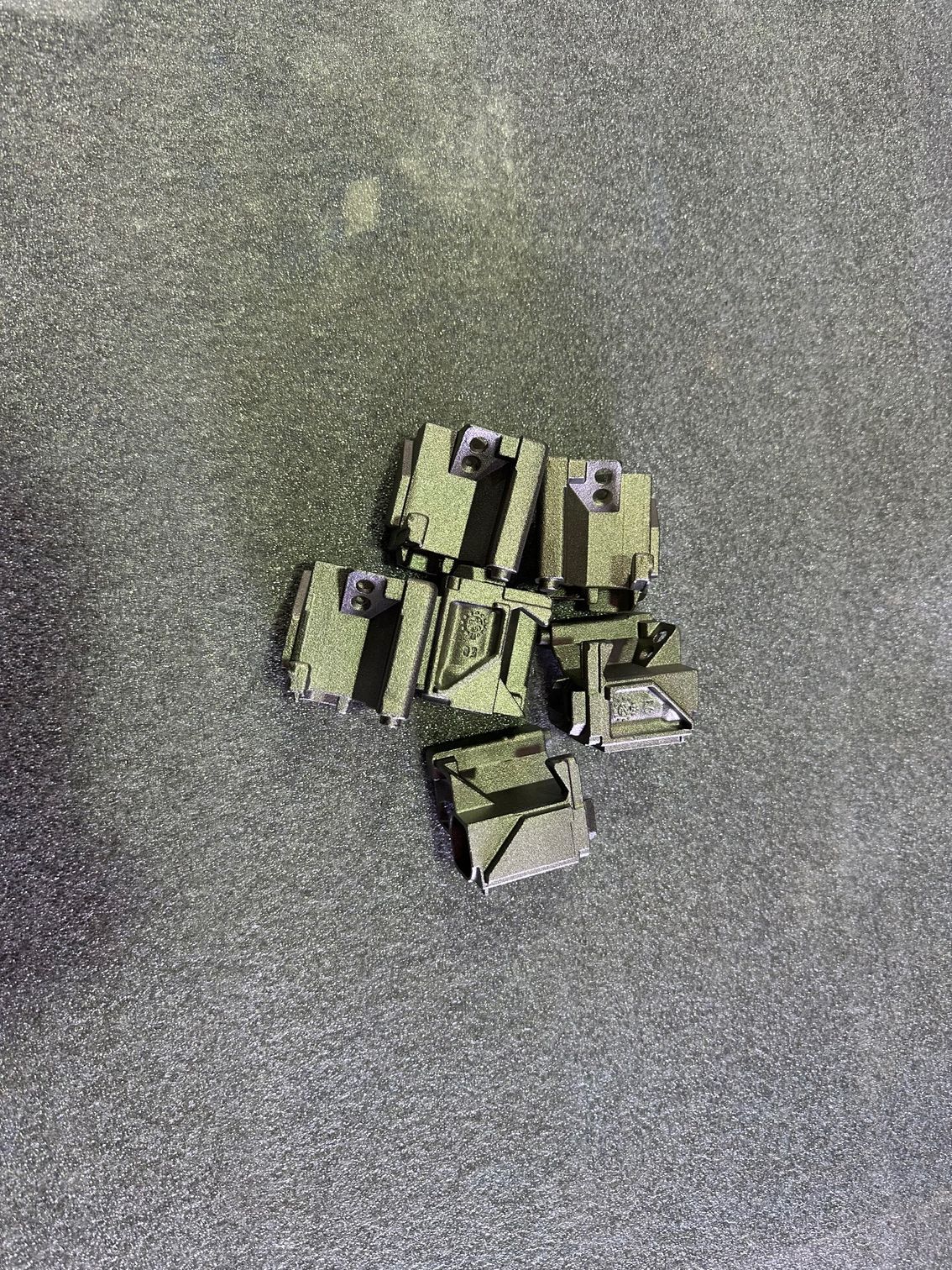 Petits objets géométriques verts regroupés sur une surface texturée gris foncé.