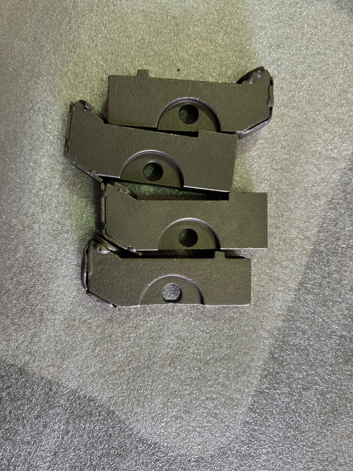 Quatre pièces mécaniques gris foncé, de forme semi-circulaire, empilées les unes sur les autres. Chacune possède un trou central.