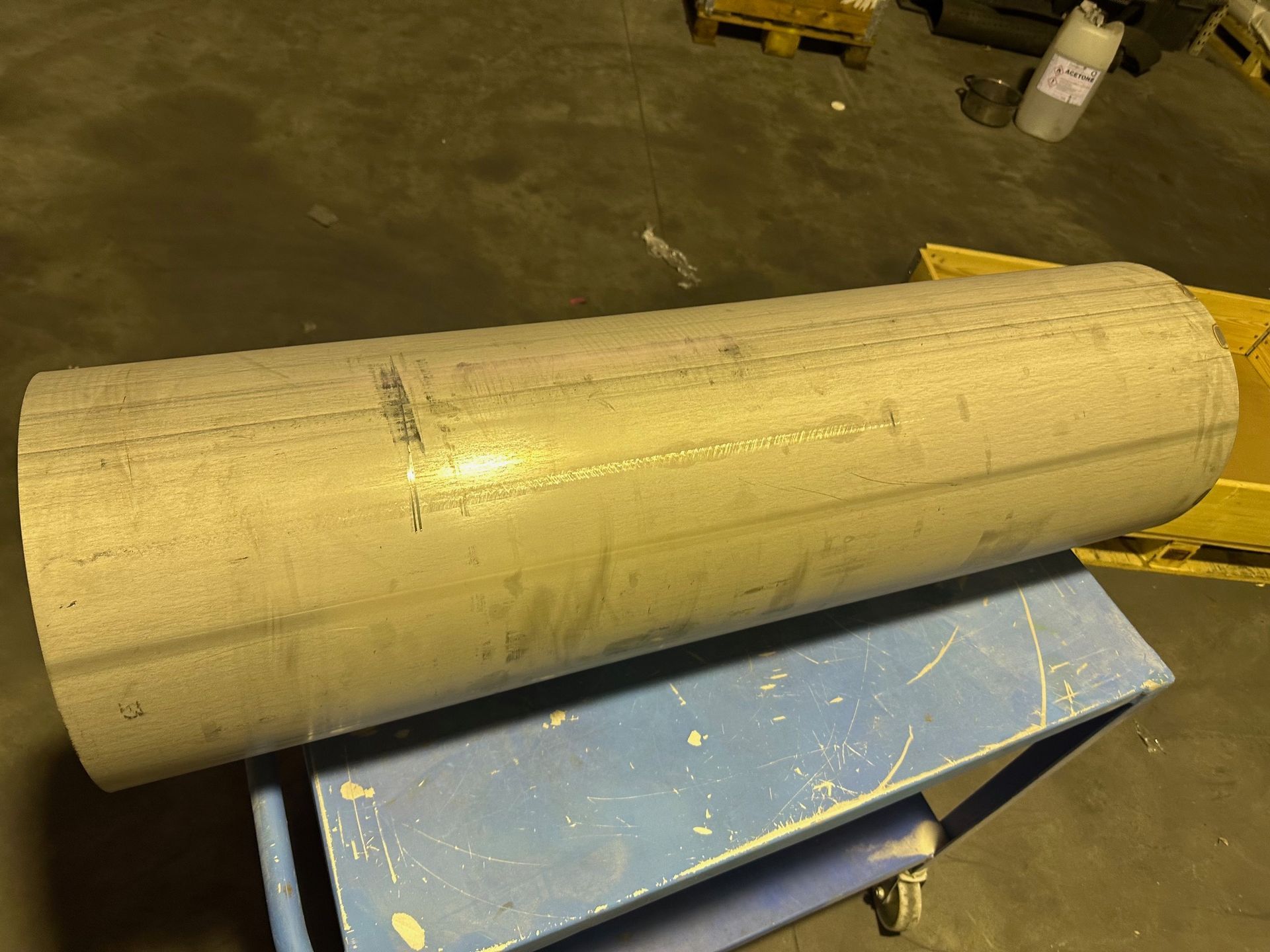 Un tuyau cylindrique en métal argenté repose sur un chariot bleu dans un environnement industriel.