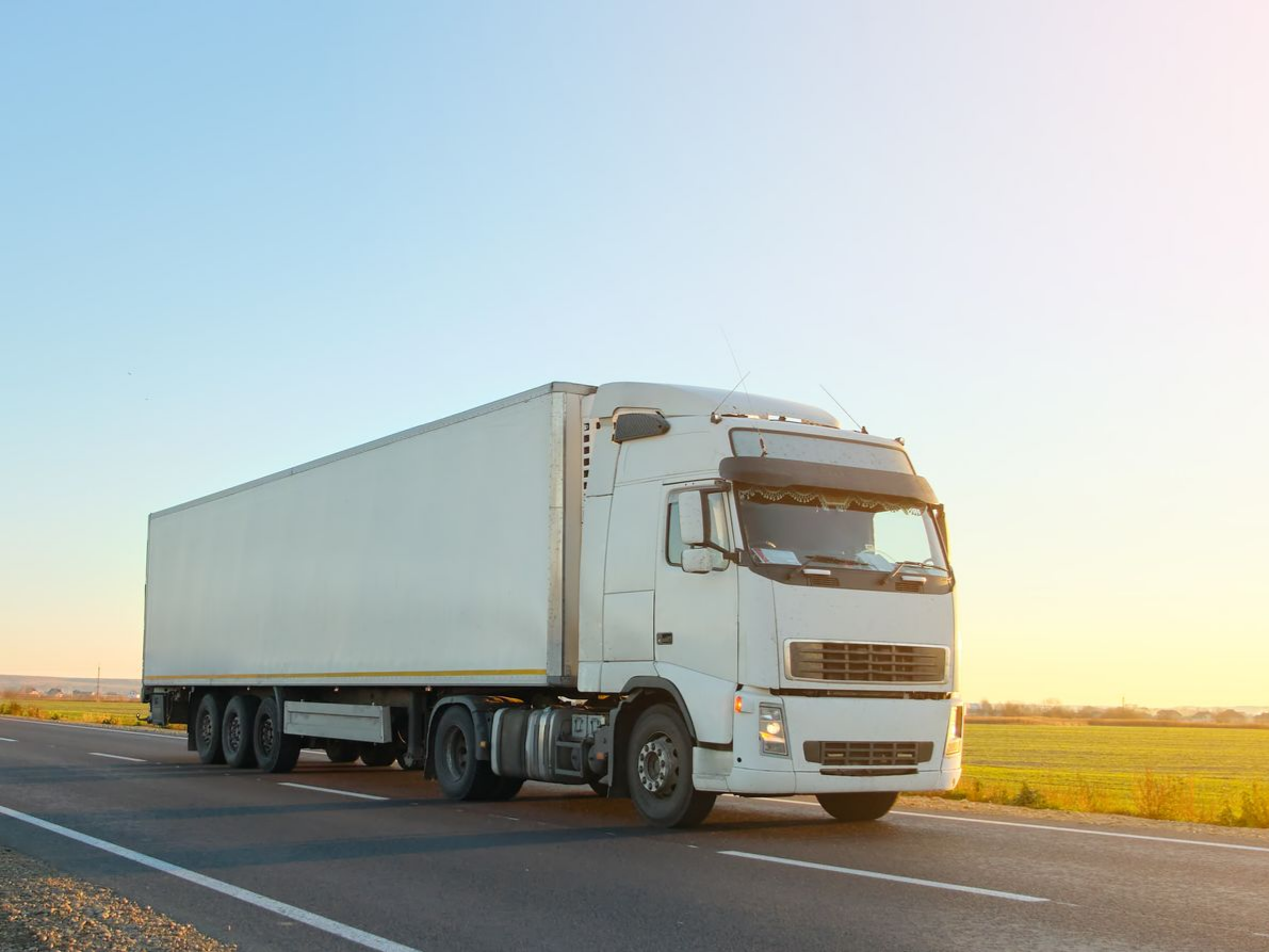 Un semi-remorque blanc circule sur une route sous un ciel d'un bleu éclatant.