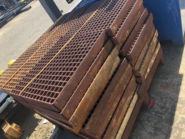 Empilement de panneaux de caillebotis métalliques rouillés sur une palette en bois à l'extérieur.