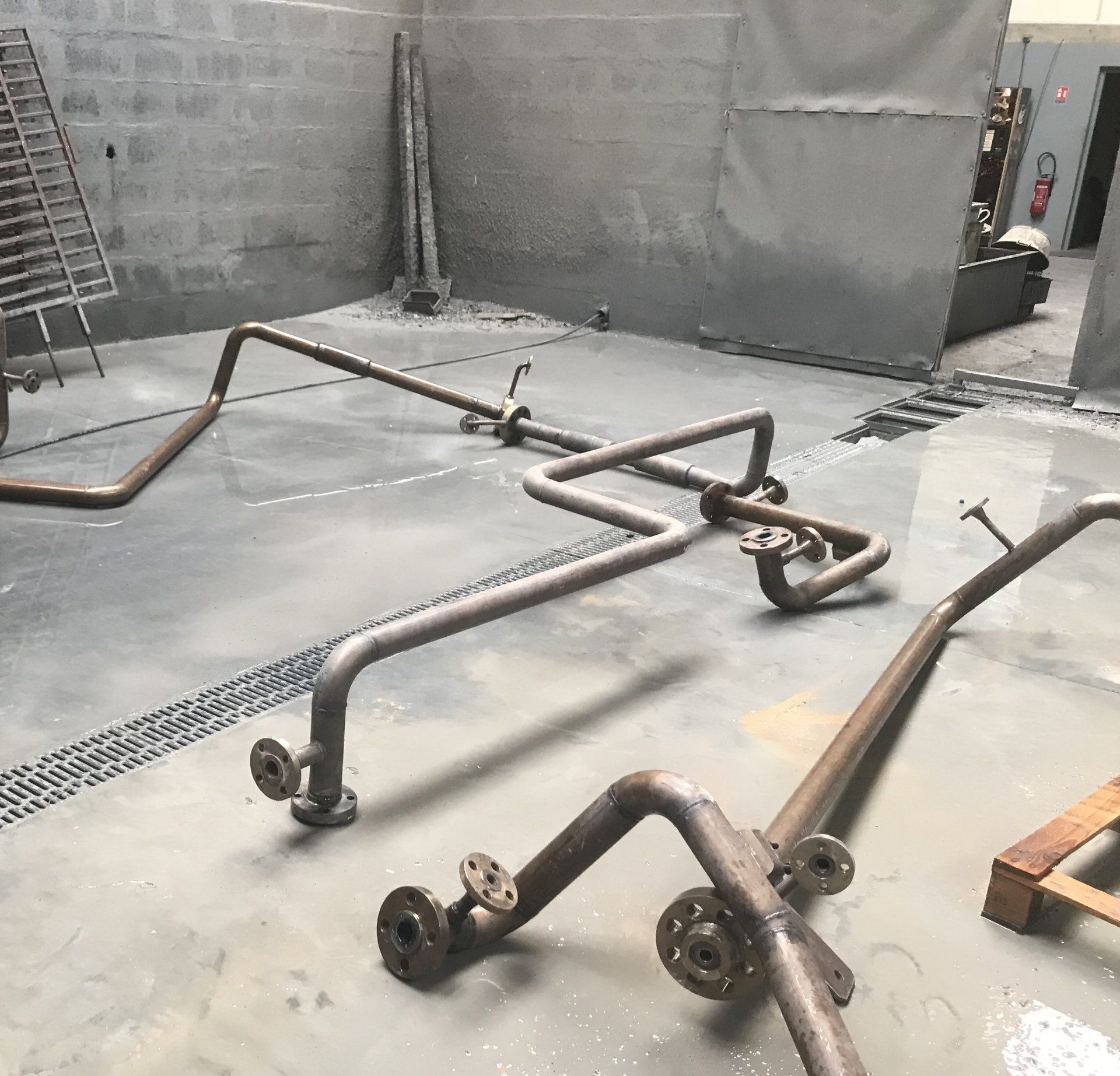 Tuyauterie métallique sur un sol en béton dans un atelier, possiblement à usage industriel.