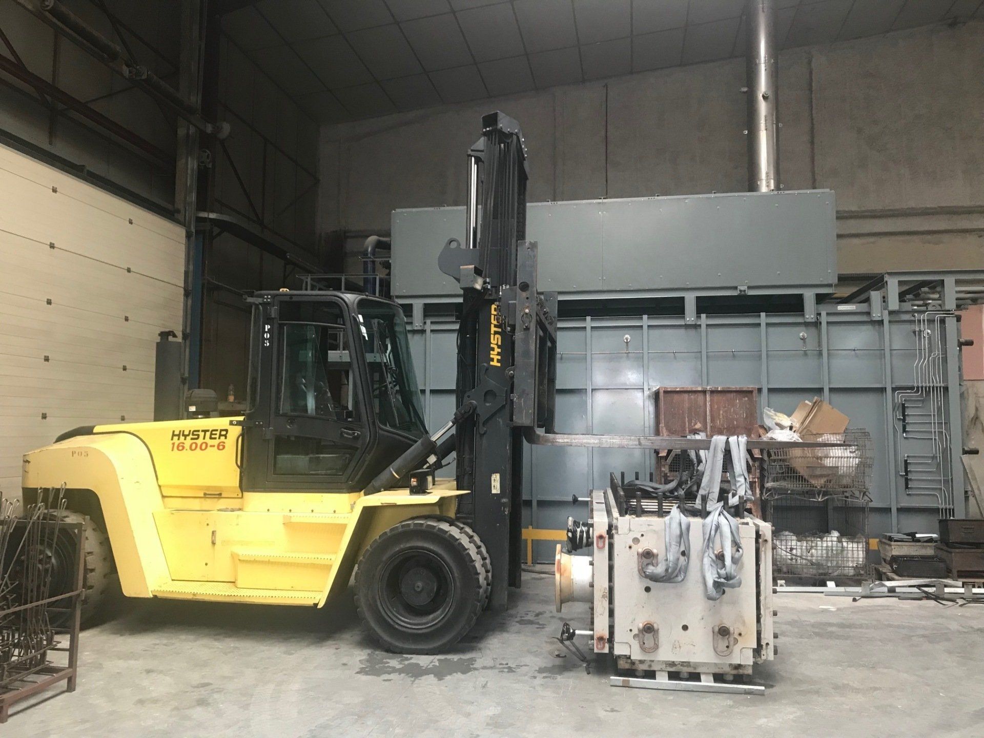 Un chariot élévateur jaune dans un environnement industriel, soulevant un conteneur métallique près d'une grande machine grise.