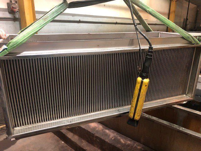 Filtre industriel en acier inoxydable suspendu par des sangles vertes, dispositif de commande jaune fixé.