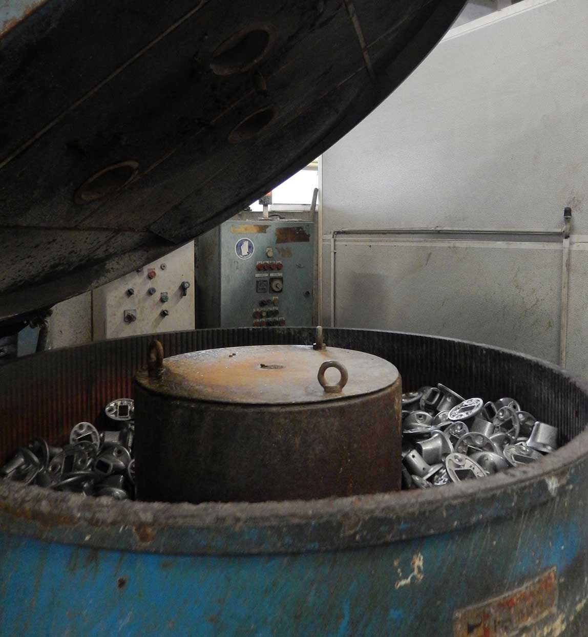 Machine de nettoyage de pièces métalliques avec un grand tambour ouvert contenant plusieurs pièces.