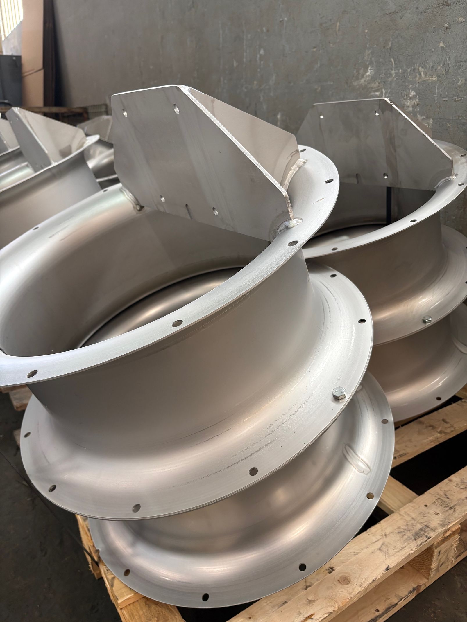 Composants métalliques industriels avec brides circulaires et plaques de montage, empilés sur une palette en bois dans un atelier.