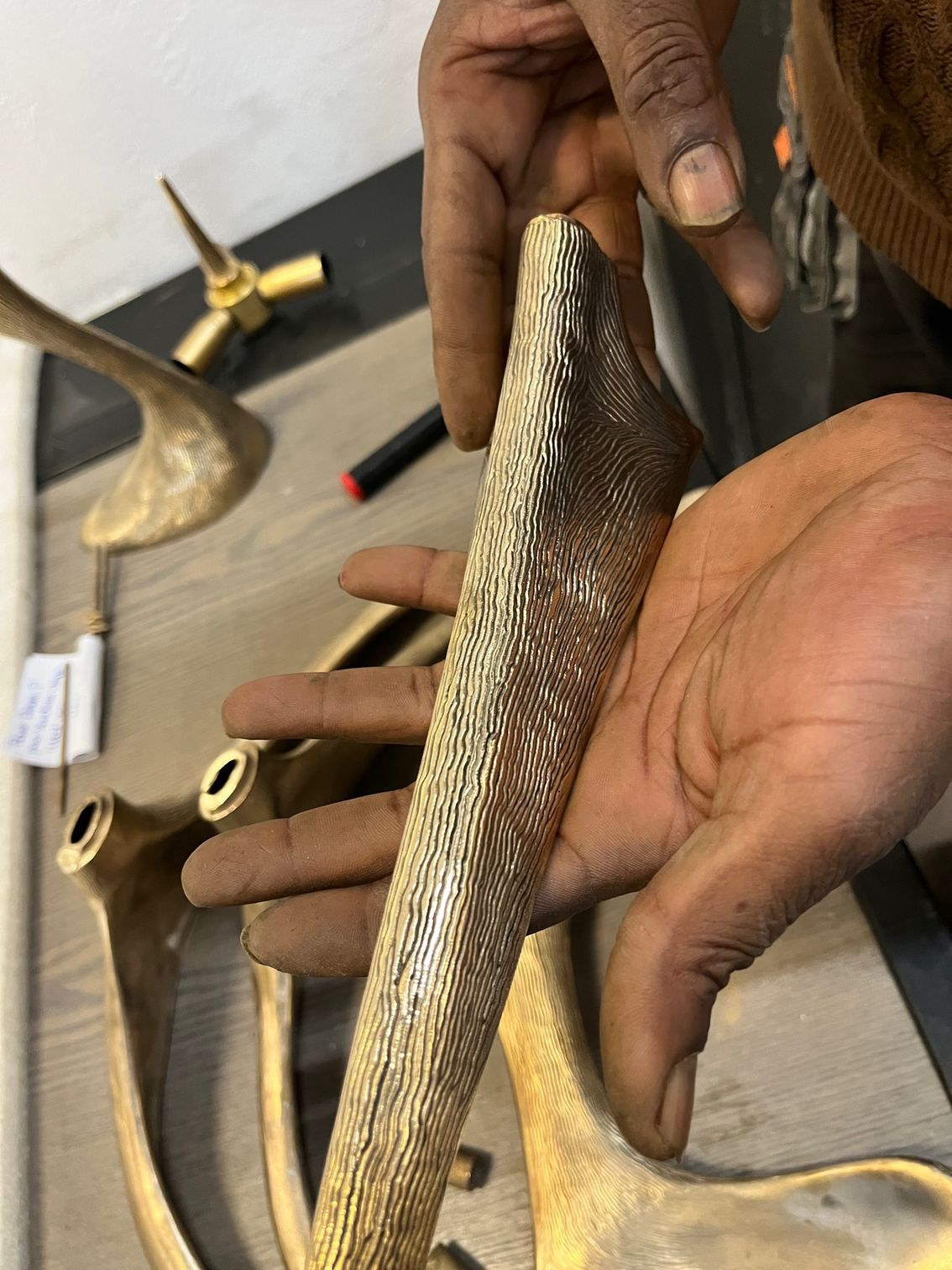 Une personne tenant un objet métallique texturé de couleur dorée, avec des objets et des outils similaires visibles sur une surface claire.