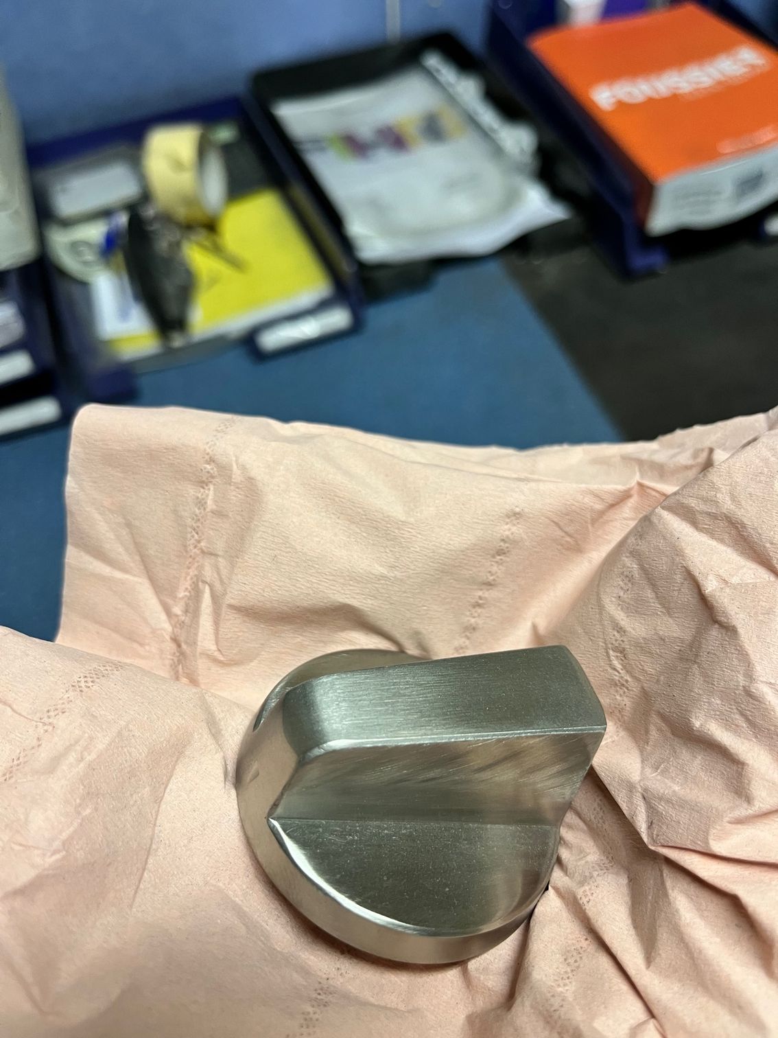 Composant de prothèse de genou en métal argenté sur du papier de soie rose.