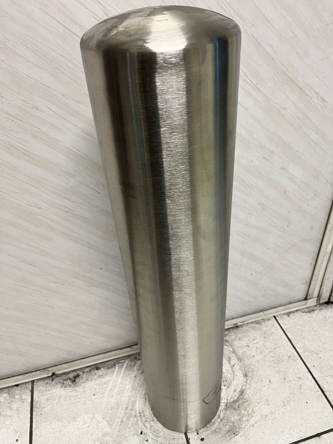 Borne cylindrique en acier inoxydable poli, à sommet arrondi, dans un intérieur carrelé.