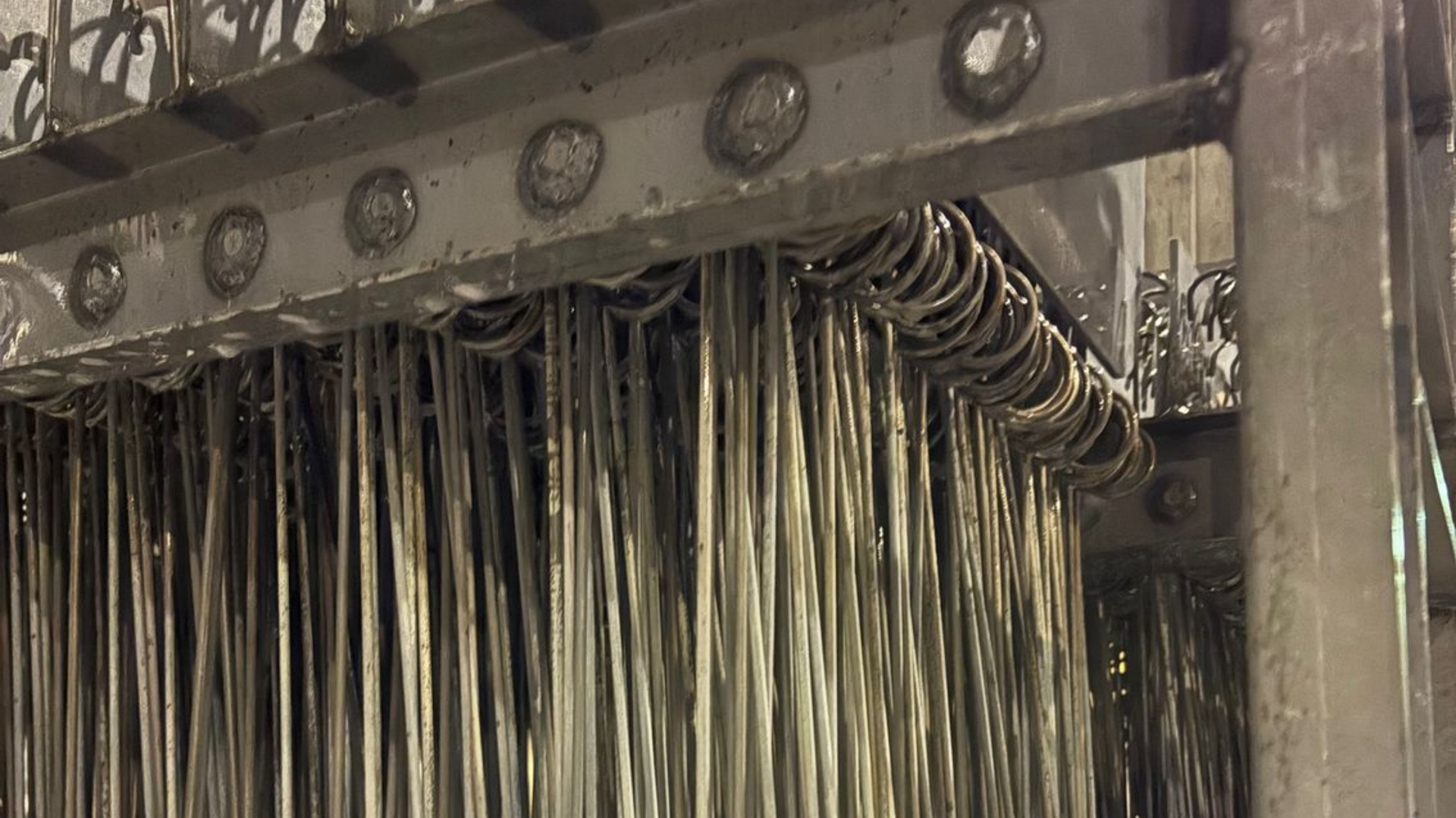 Un support industriel métallique maintient des rangées de longues et fines tiges métalliques verticales suspendues à des anneaux circulaires.