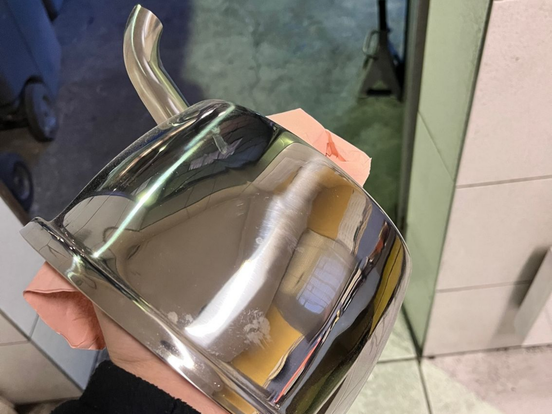 Une main tenant un embout d'échappement en métal brillant et courbé, reflétant l'environnement.