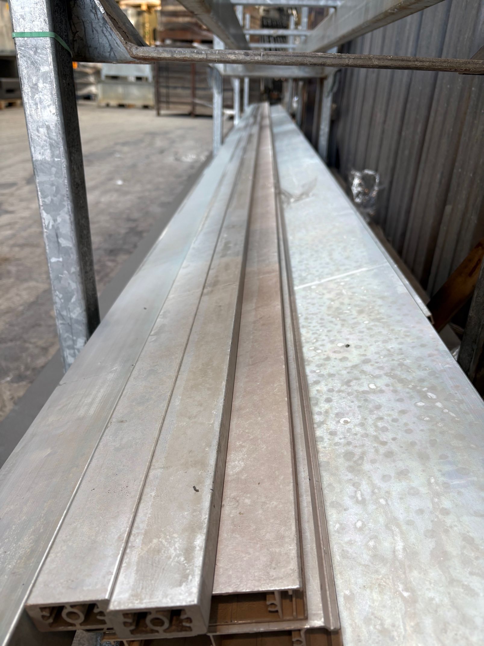Une pile de longs profilés industriels en aluminium reposant sur des étagères métalliques dans un entrepôt.