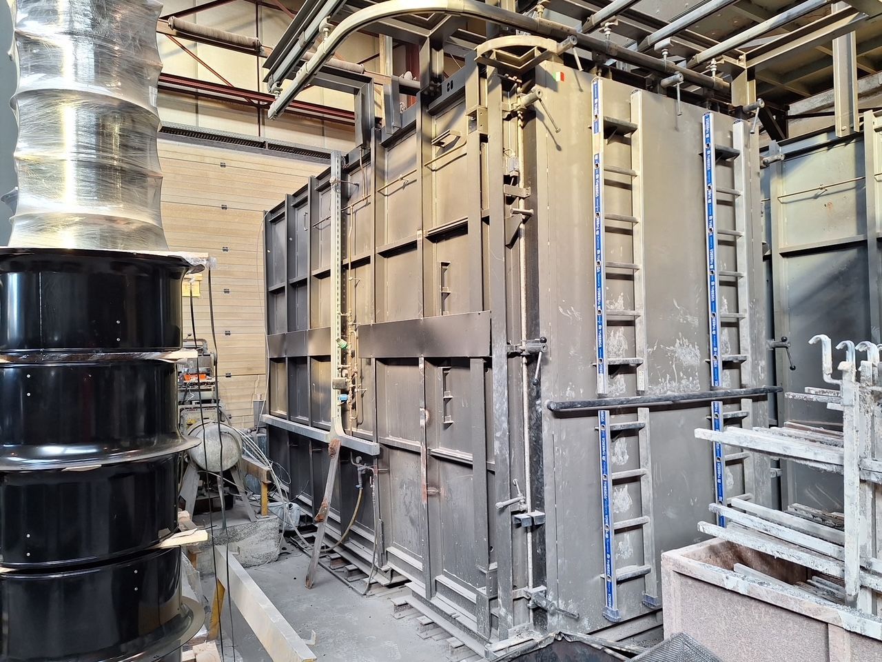 Un grand four industriel en acier se dresse dans une usine, arborant des marquages ​​de sécurité bleus verticaux et des échelles intégrées.