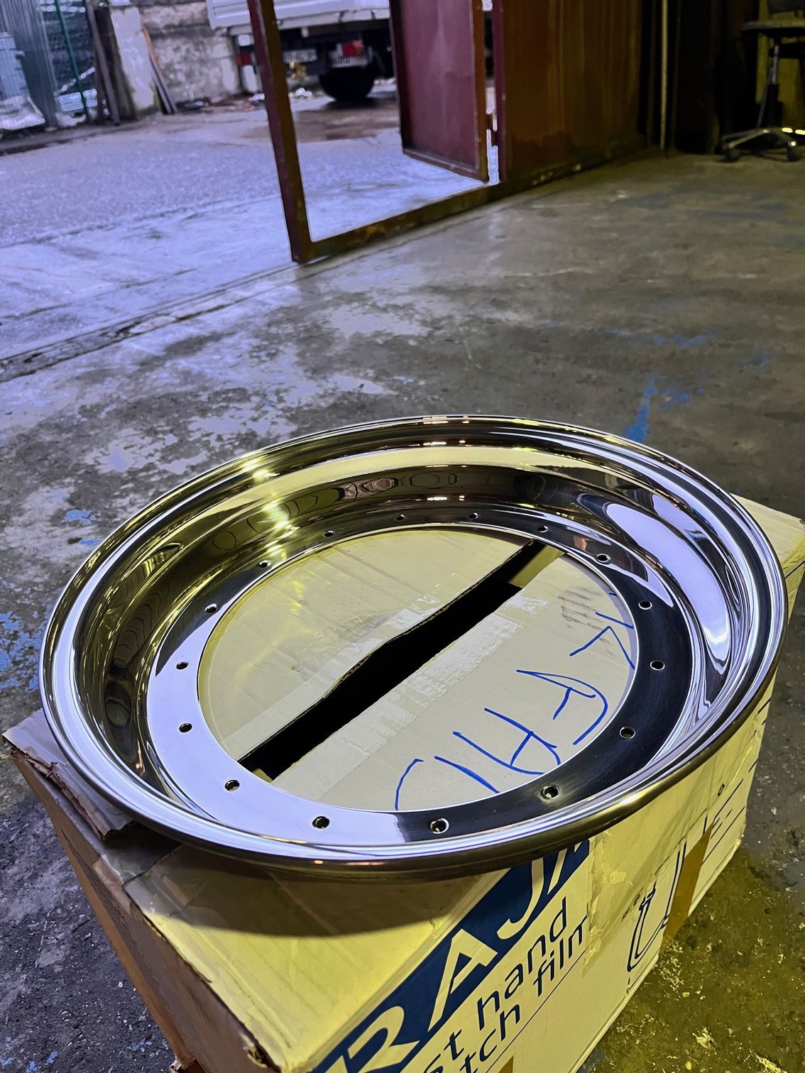 Jante de voiture chromée brillante posée sur une boîte en carton dans un environnement industriel.