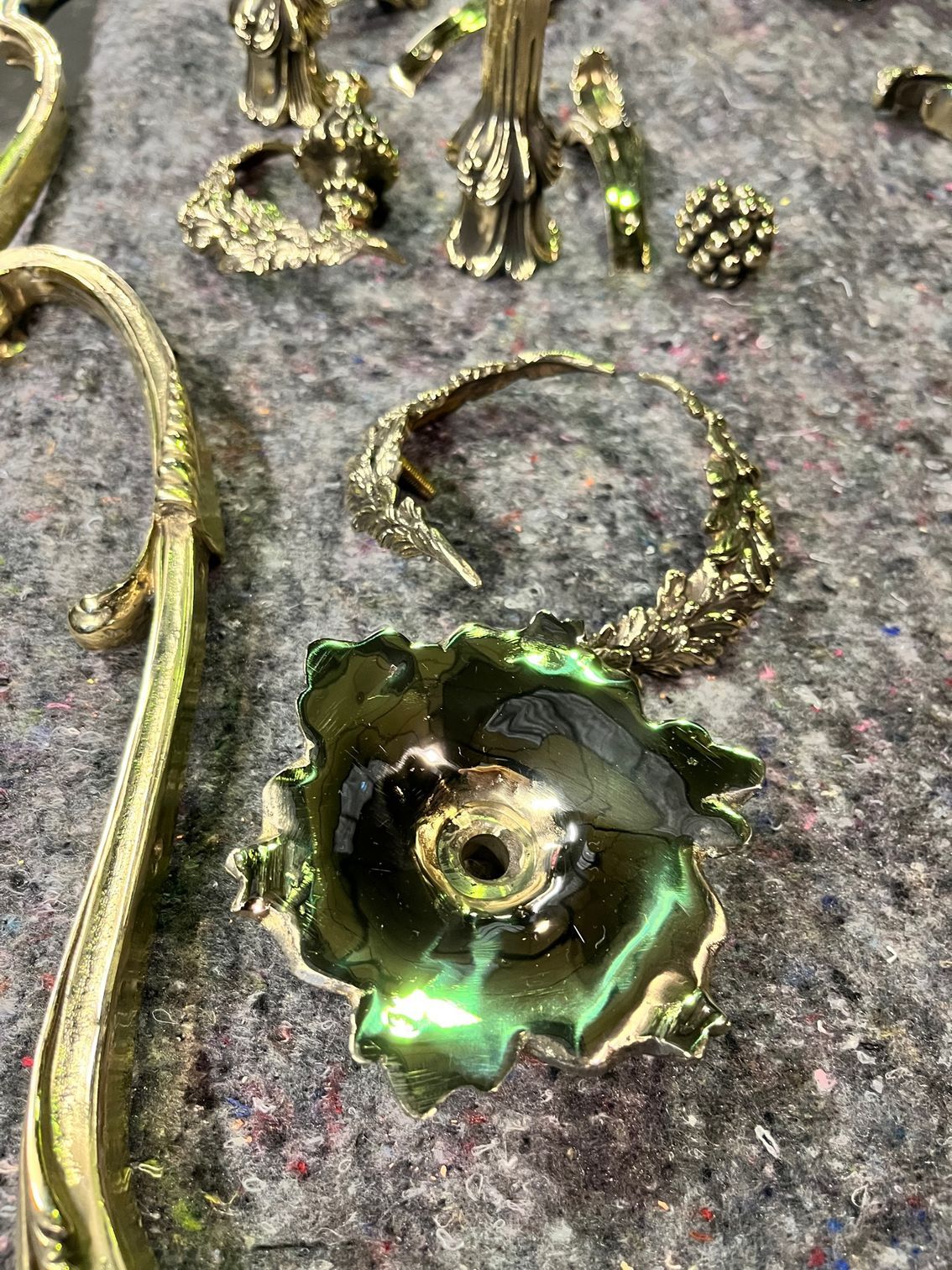 Gros plan sur des pièces métalliques dorées ornementées, notamment une forme de fleur et un anneau incurvé, sur une surface grise.