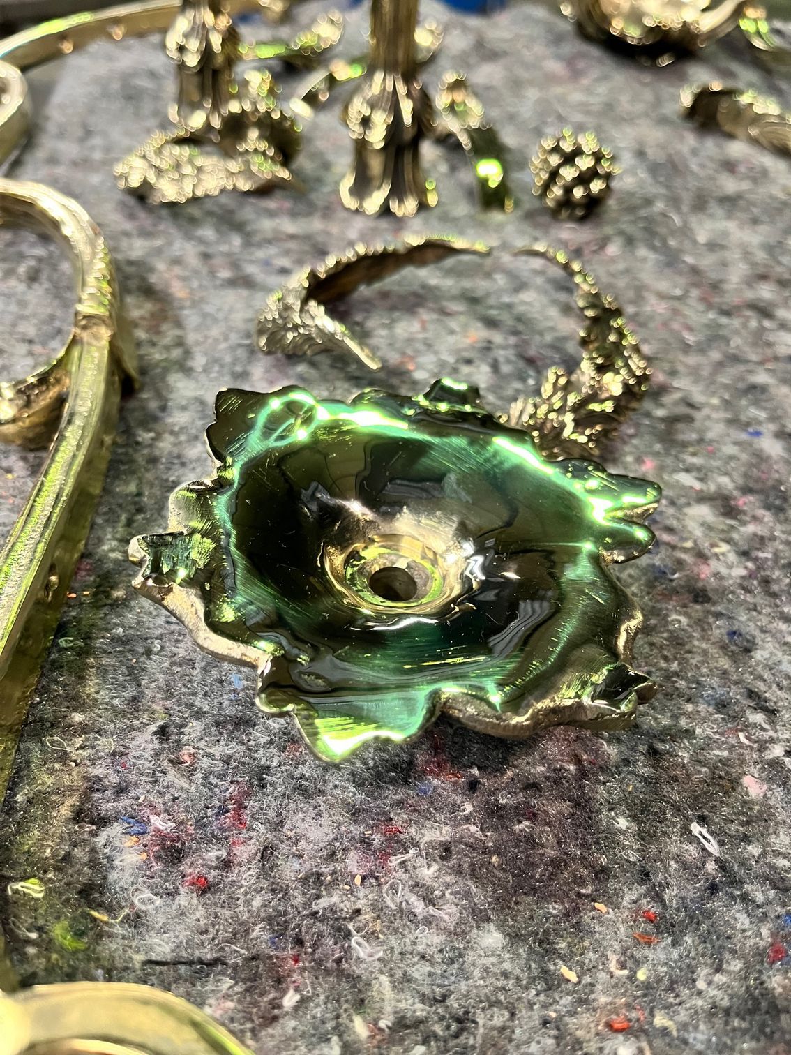 Évier en métal émaillé vert en forme de fleur avec un rebord couleur laiton, posé sur une surface grise avec d'autres objets artisanaux en métal.