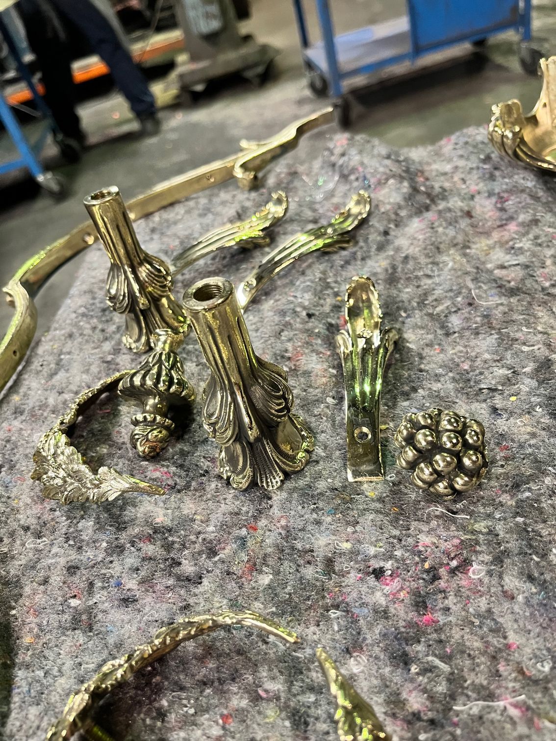 Pièces de quincaillerie ornementales en métal doré sur une surface en feutre gris, probablement destinées à la restauration de meubles.