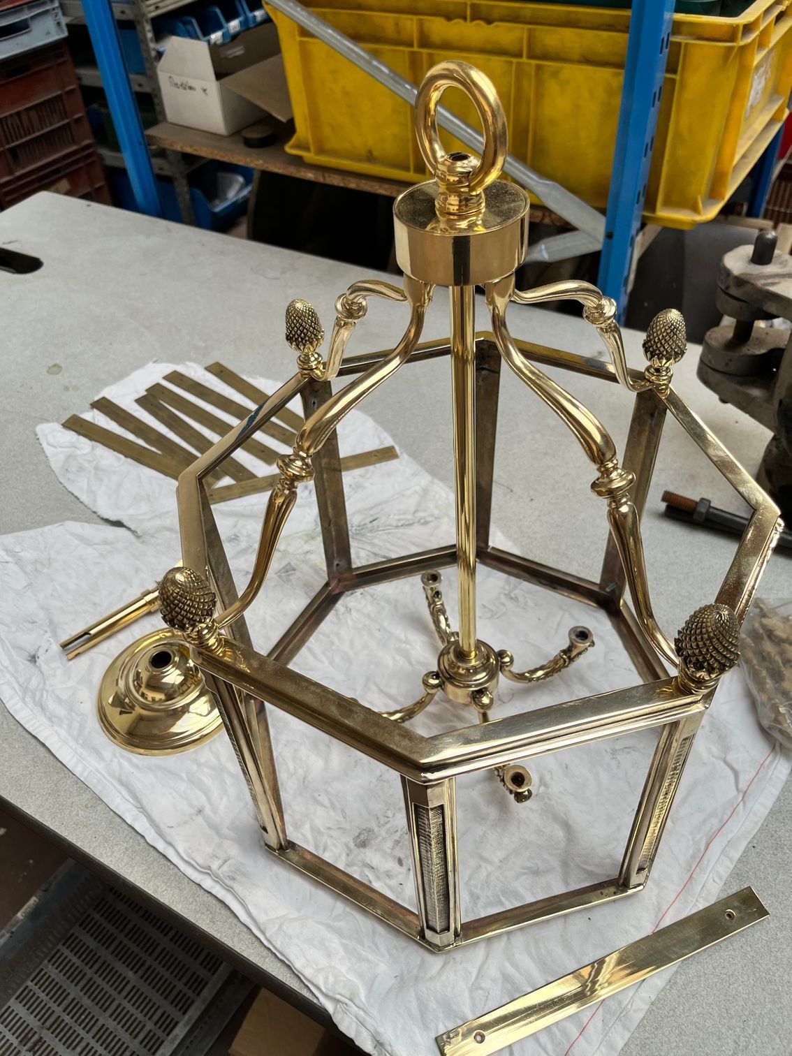 Lanterne octogonale dorée avec fleurons, anneau et tige centrale, posée sur une nappe blanche sur une table.