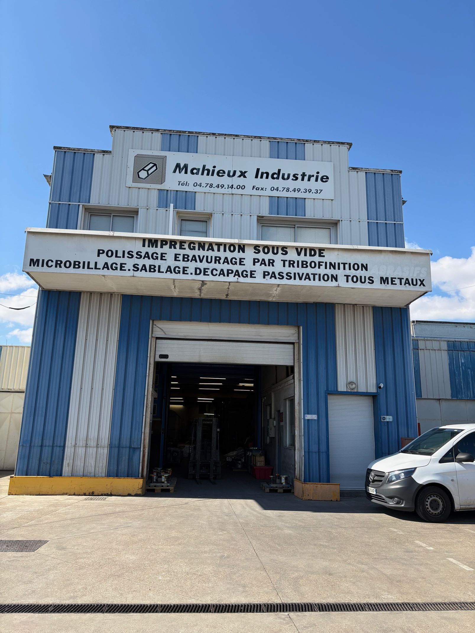 Bâtiment industriel gris avec quai de chargement ouvert et signalétique BREF. Rayonnages métalliques visibles.