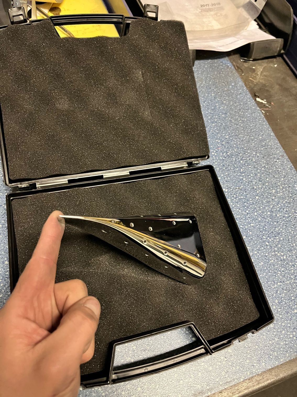 Main tenant une pince à épiler sortie d'un étui noir ouvert doublé de mousse.