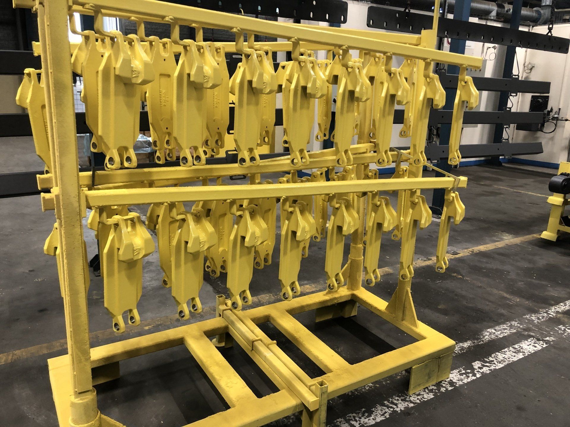 Un rack métallique jaune supportant de nombreux composants identiques peints en jaune, suspendus dans un environnement d'usine.