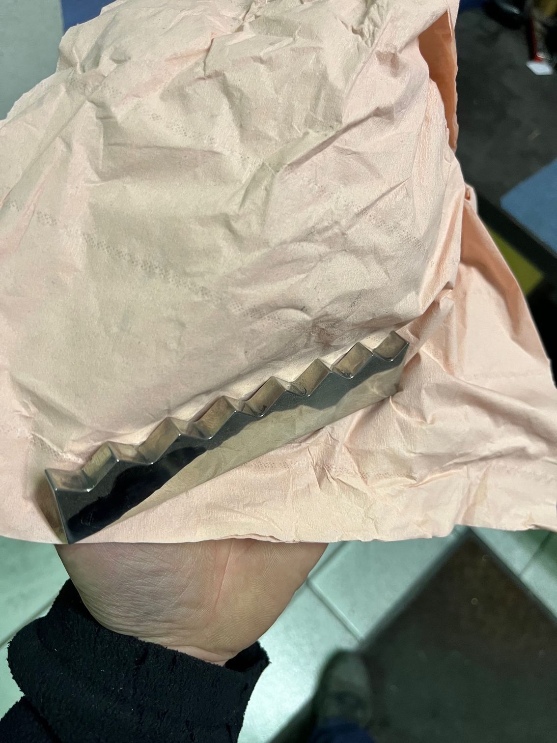 Main tenant un objet métallique aux bords ondulés, enveloppé dans du papier de soie rose.