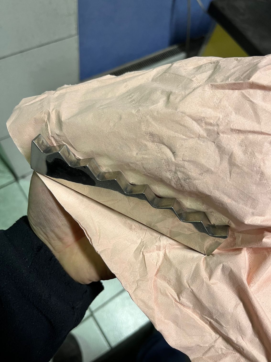 Main tenant une pièce de métal en zigzag enveloppée dans du papier rose.