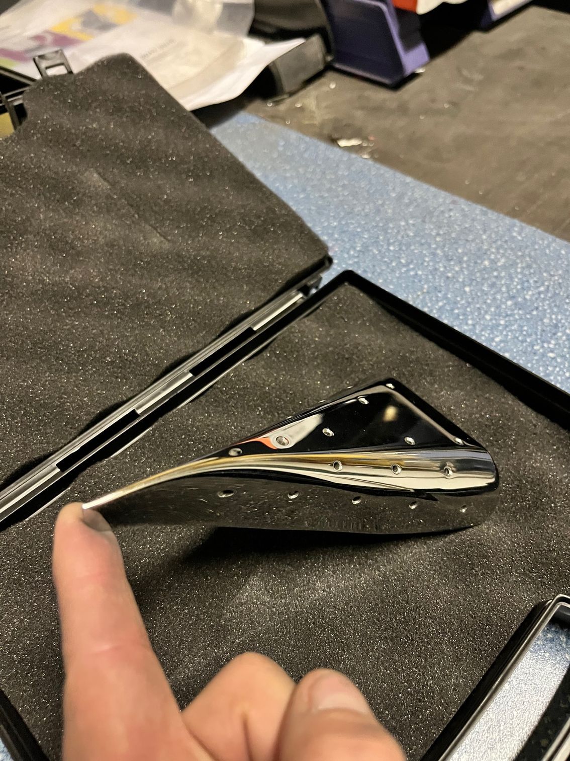 Une poignée de portière chromée repose dans un étui de protection. Un doigt désigne la poignée.