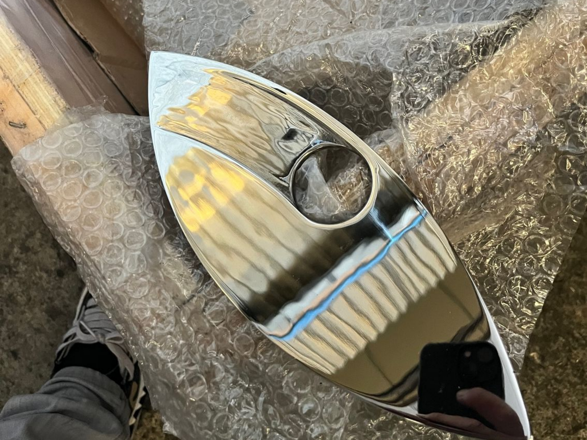 Panneau métallique ovale et brillant percé d'un trou rond. La lumière réfléchie crée des motifs rayés et des reflets bleus.