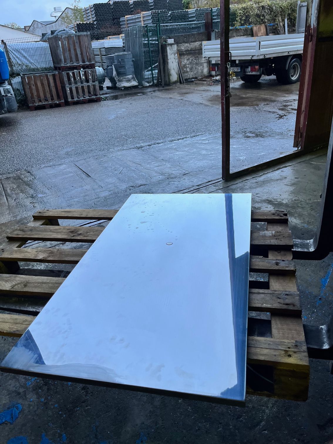 Une grande feuille de matériau réfléchissant repose sur une palette en bois à l'extérieur, sur une surface humide.