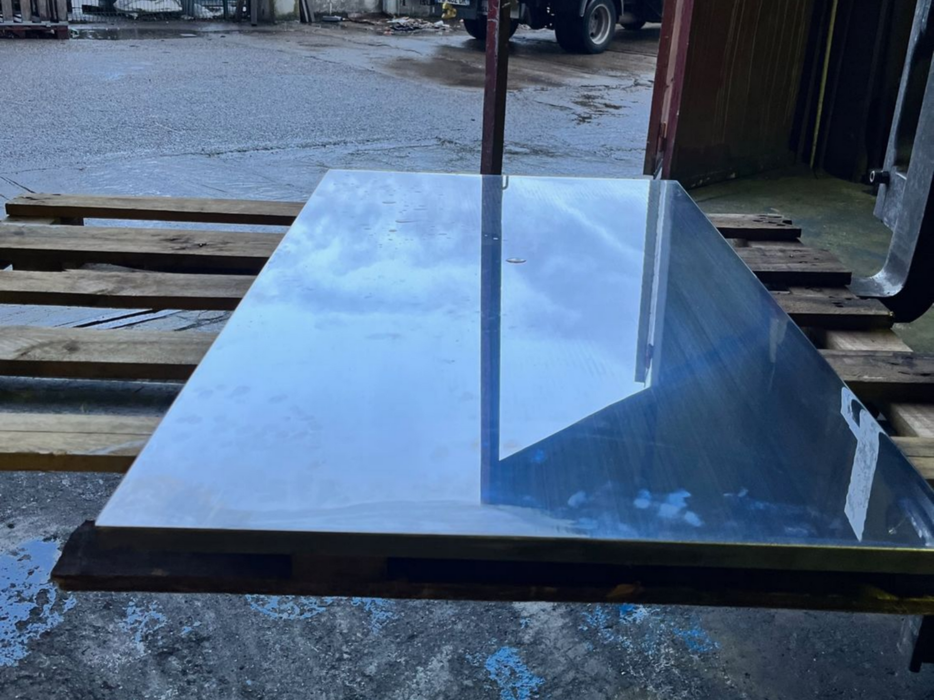 Grande surface réfléchissante sur une palette en bois, reflétant le ciel et les environs.