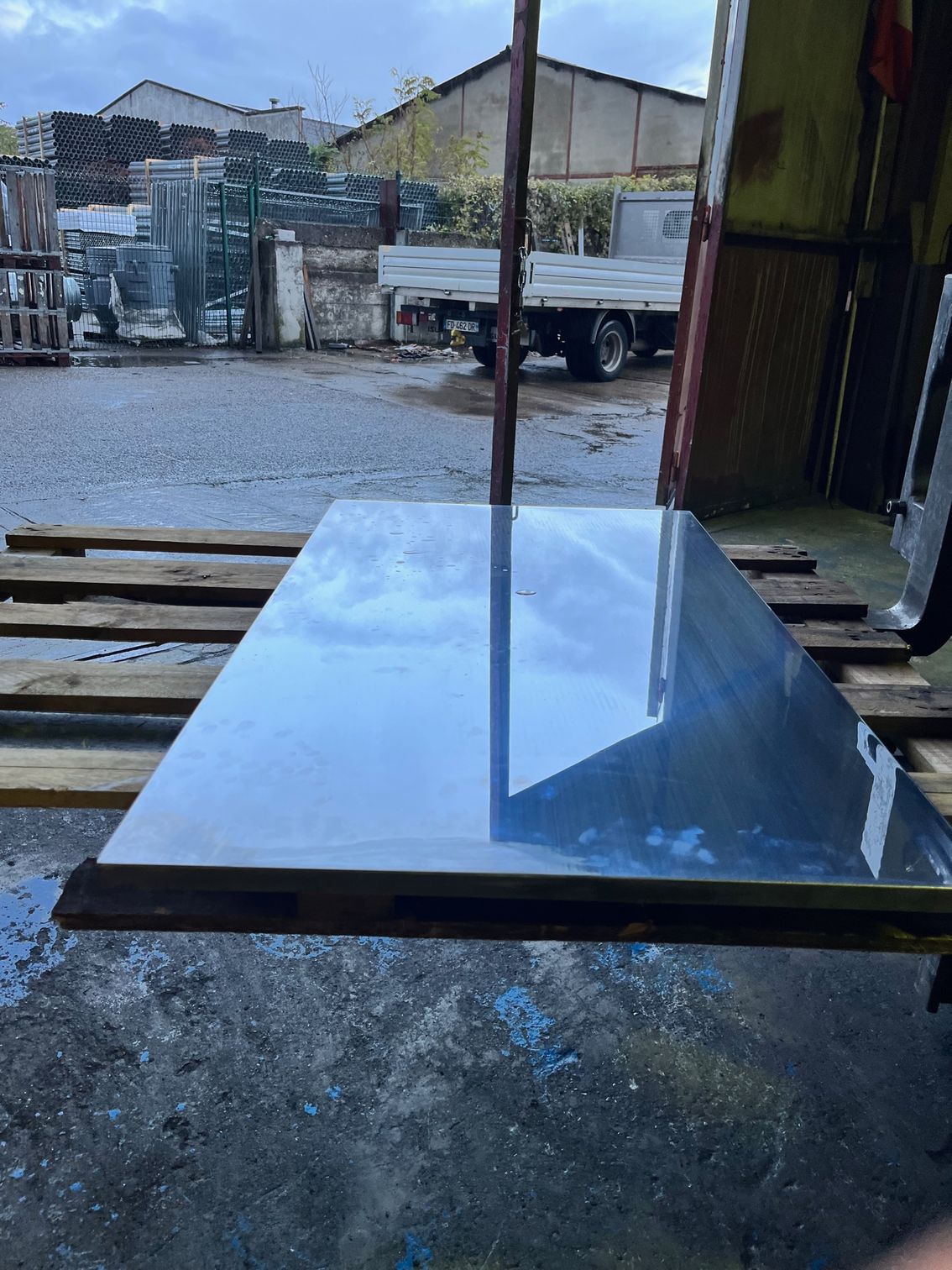 Grande plaque de verre noire et réfléchissante sur supports en bois dans une zone industrielle, avec un camion en arrière-plan.