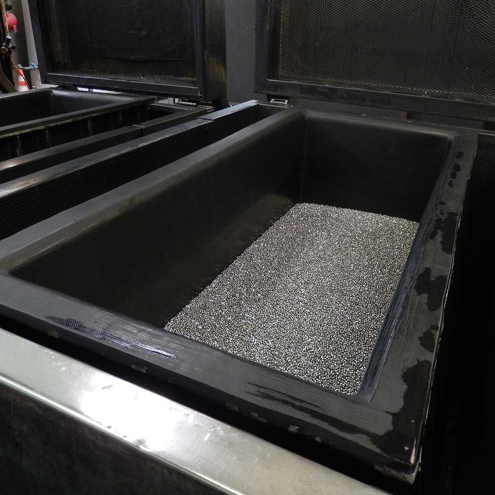 Un réservoir rectangulaire rempli de petits morceaux de métal gris, probablement utilisé dans un processus industriel.