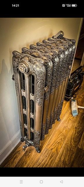 Radiateur ancien orné contre un mur beige et un parquet.